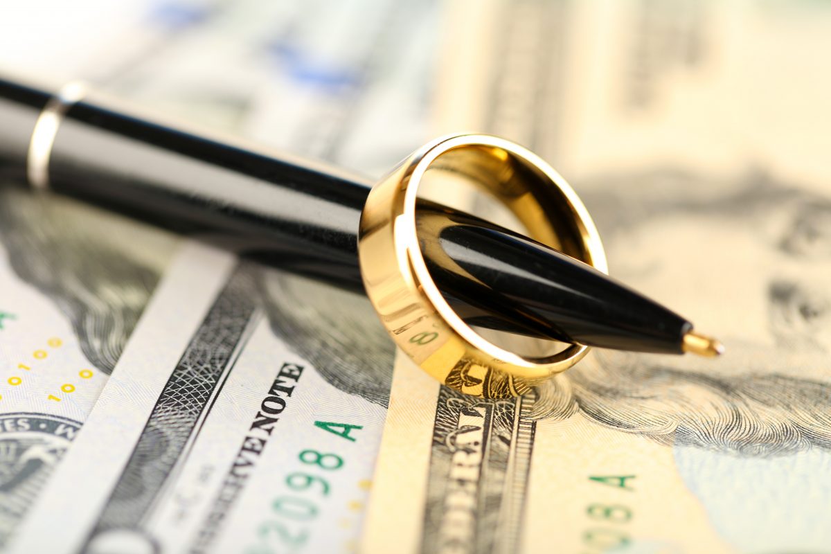 Wedding band on pen with money in background when needing Family Law Firm Sterling Heights.